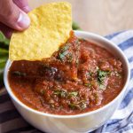 A bowl of salsa with a chip dipping into it.