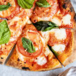 An above view of a tomato margherita pizza with fresh basil.