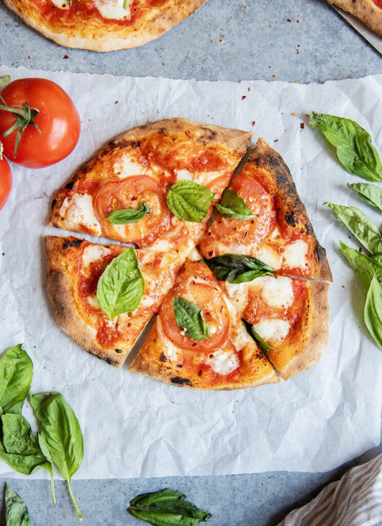 An above view of a sliced Margherita pizza with fresh basil on top.