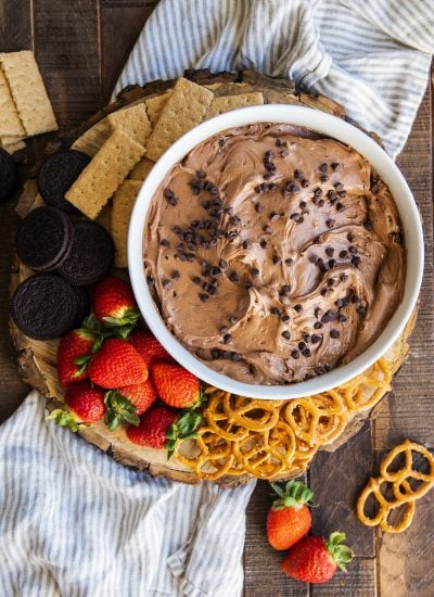 A bowl of brownie batter dip topped with chocolate chips and surrounded by dippers like pretzels, strawberries, and cookies.