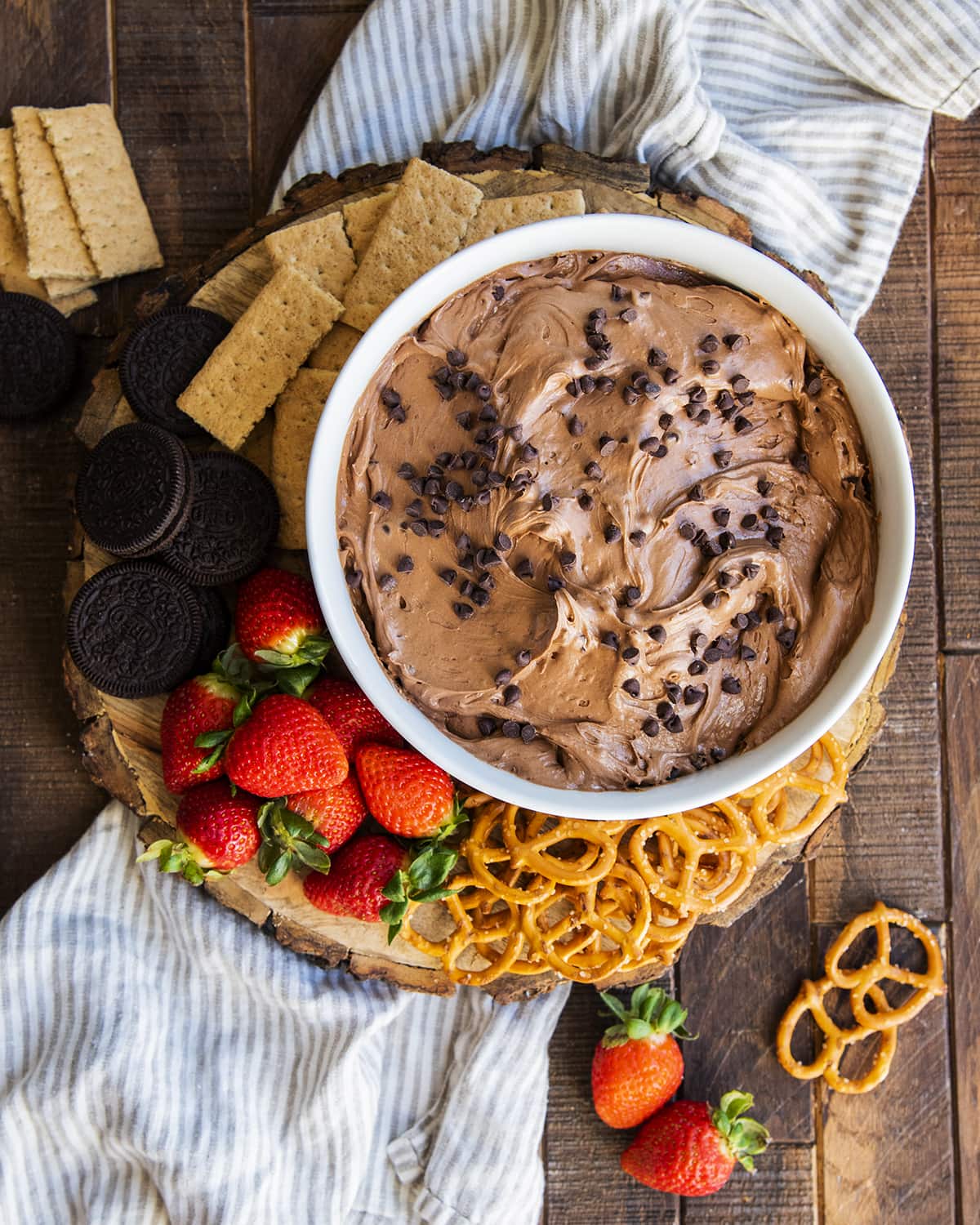 A bowl of brownie batter dip topped with chocolate chips and surrounded by dippers like pretzels, strawberries, and cookies.