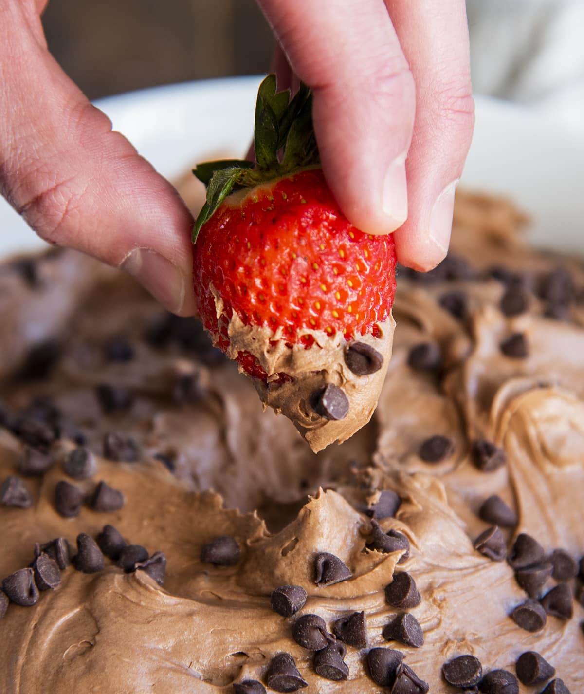 A hand holding a strawberry that is half way covered in brownie batter dip.