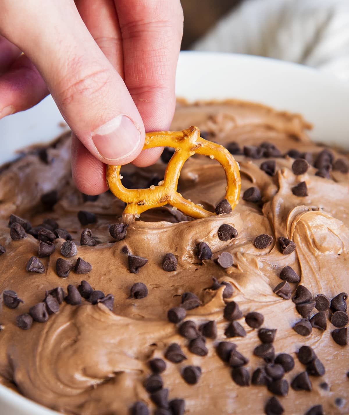 A hand dipping a pretzel into brownie batter dip.