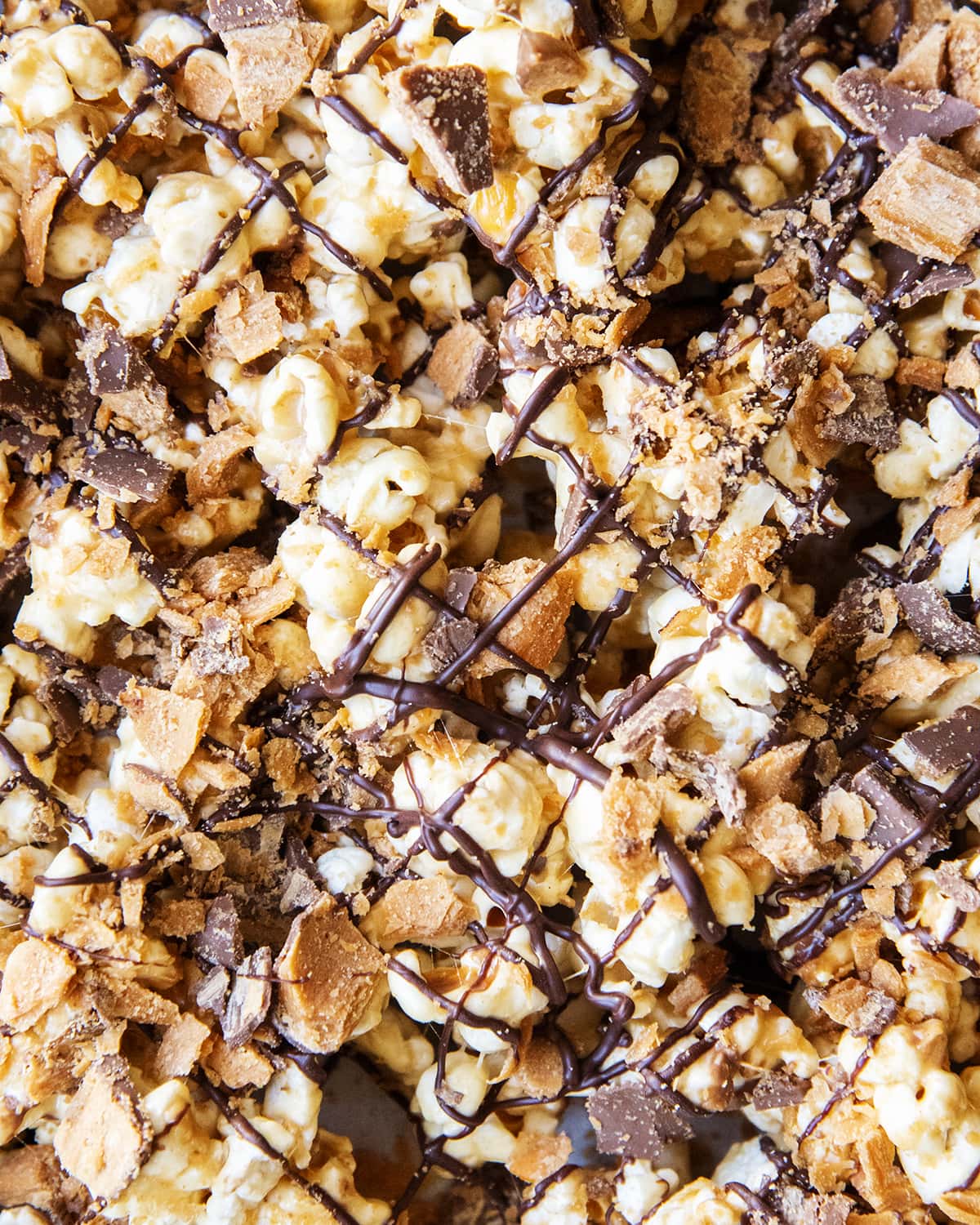 A close up of peanut butter popcorn topped with Butterfinger pieces and drizzled with chocolate.