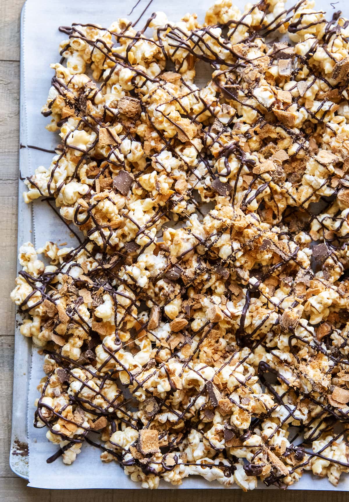 A baking pan topped with Butterfinger popcorn drizzled with melted chocolate.