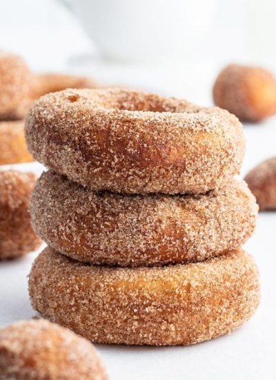 A stack of three cinnamon sugar donuts with more donuts behind them.