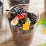 A glass cup of chocolate pudding and oreos, with candy worms in it.