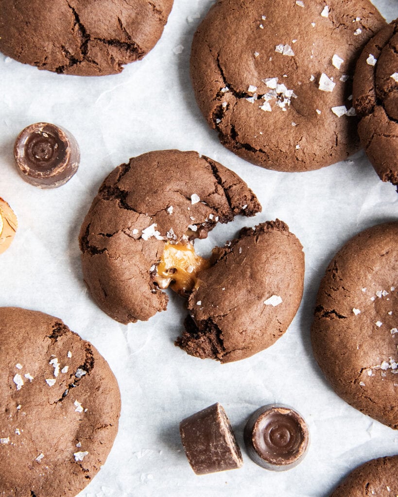 A chocolate cookie split in half showing gooey caramel in the center.