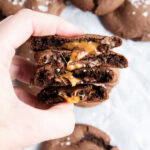 A hand holding four halves of chocolate cookies, with a gooey rolo caramel center.