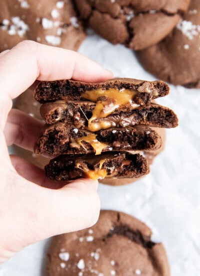 A hand holding four halves of chocolate cookies, with a gooey rolo caramel center.