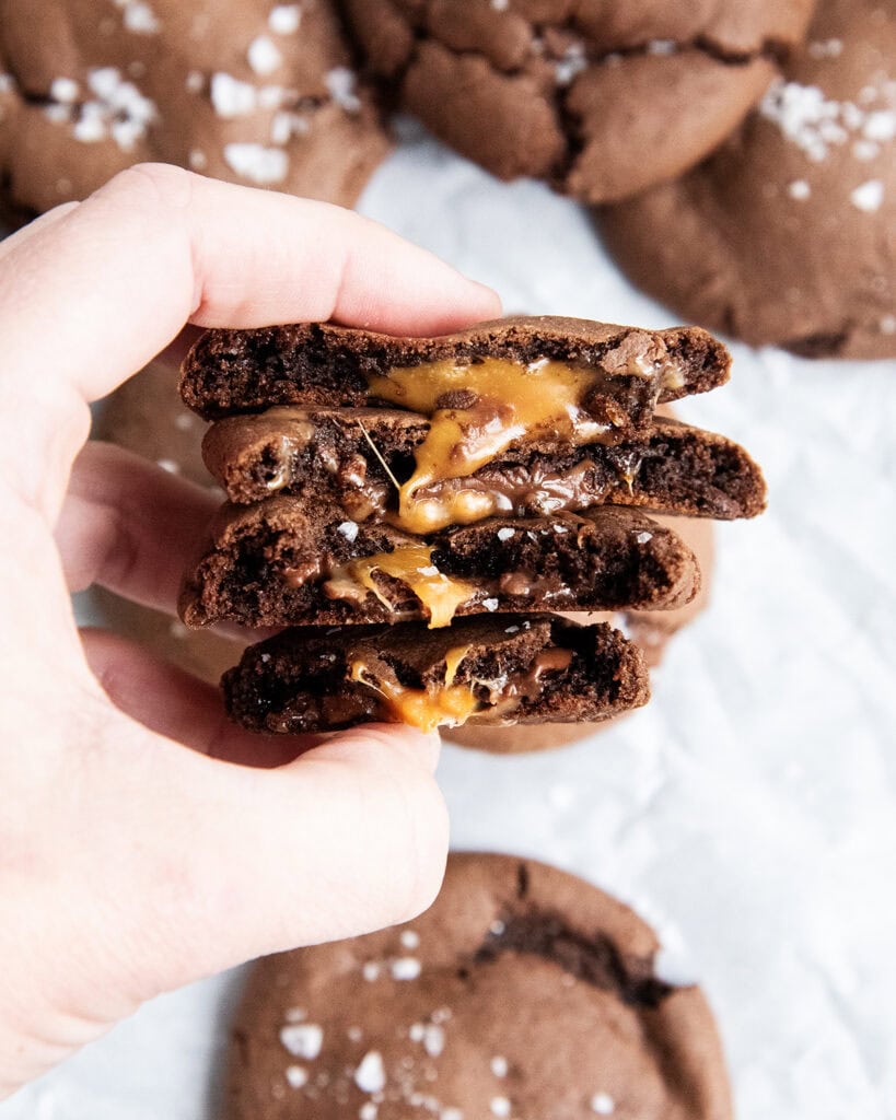 A hand holding four halves of chocolate cookies, with a gooey rolo caramel center.