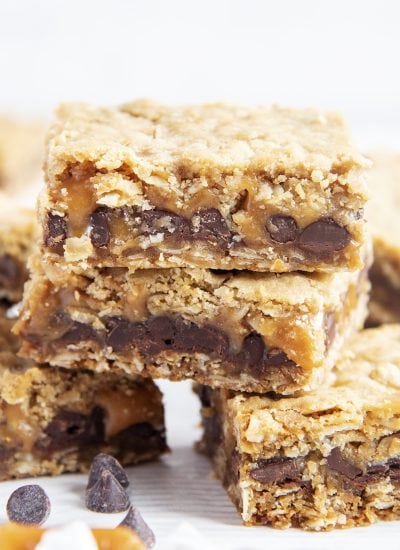 A close up of a pile of carmelitas bars, with layers of oatmeal on each side and chocolate and caramel in the middle.