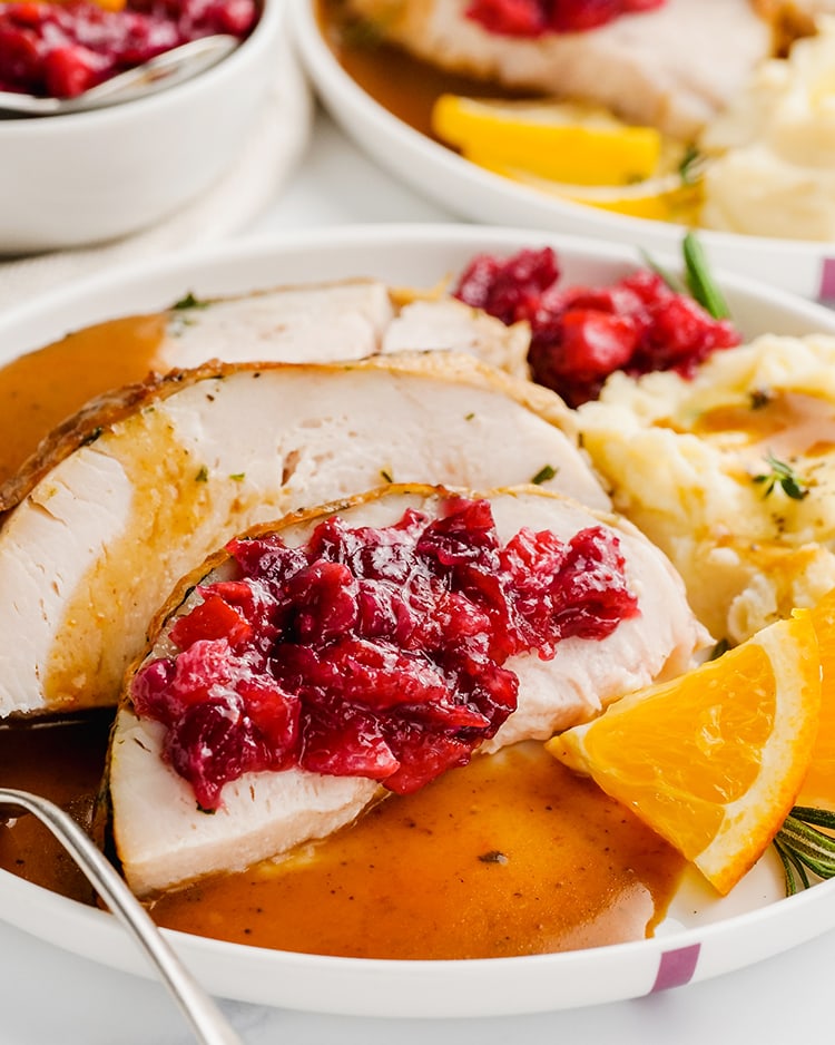 A plate of turkey topped with cranberry orange sauce and mashed potatoes.