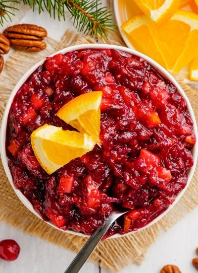 A bowl of cranberry sauce topped with a couple small orange slices with a spoon in the bowl.