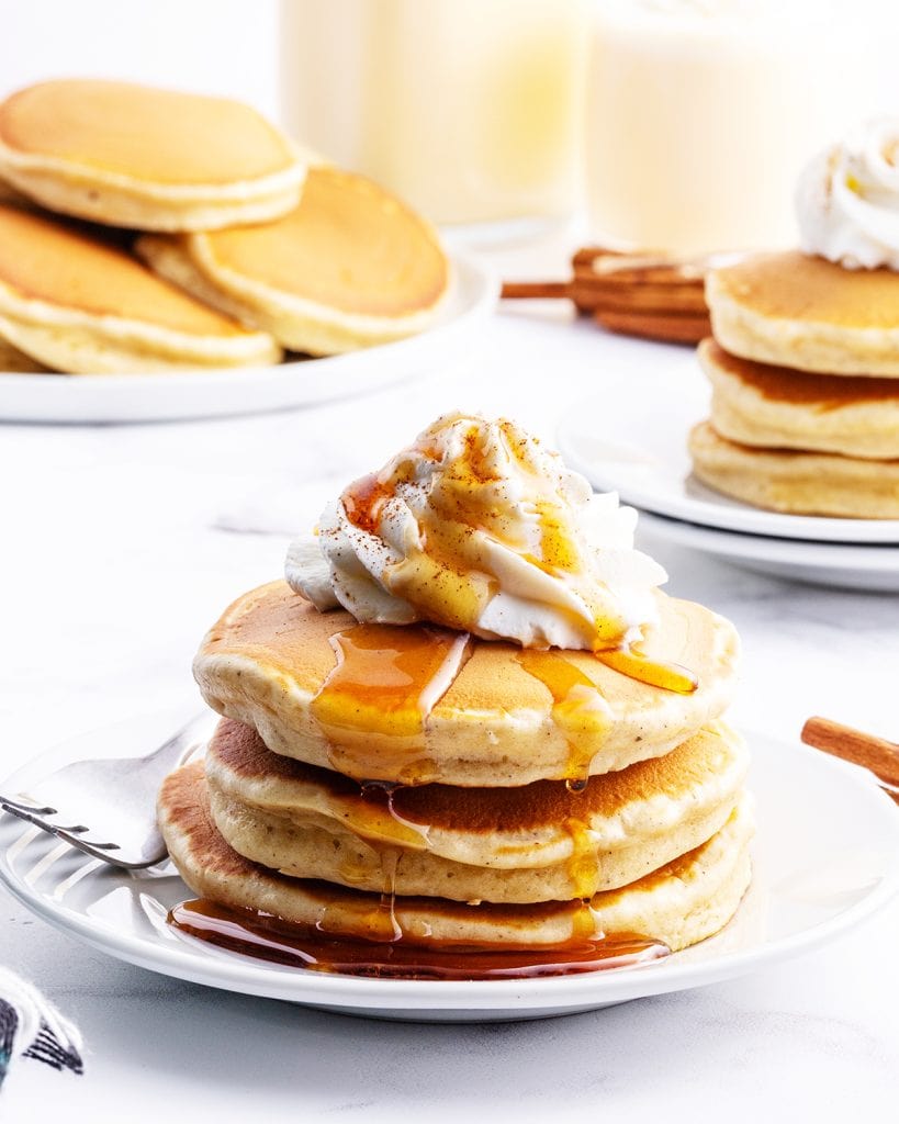 A stack of four pancakes on a plate topped with whipped cream and syrup.