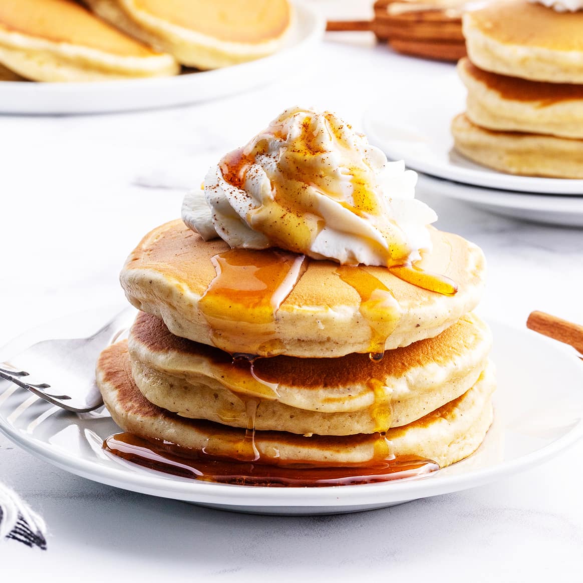 A stack of pancakes on a plate topped with whipped cream.
