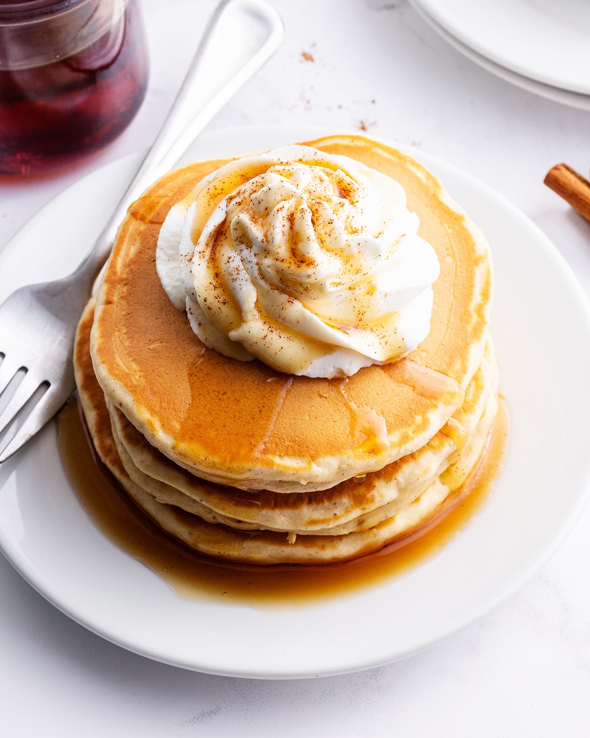 Eggnog pancakes on a plate topped with syrup and whipped cream.