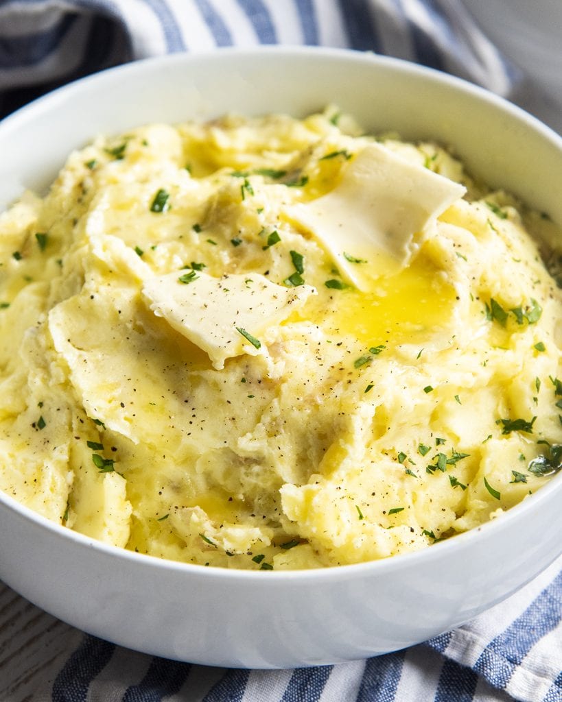 A bowl of mashed potatoes topped with butter, on top of a blue and white striped cloth.