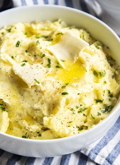 Mashed potatoes in a white bowl topped with melted butter and fresh parsley.