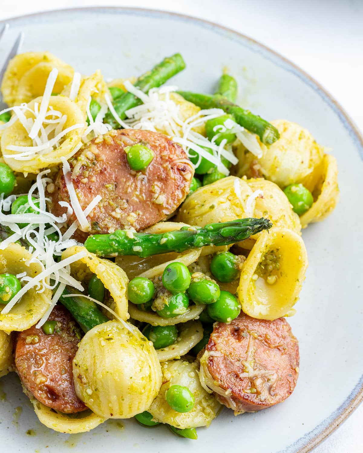 A close up of a plate of chicken sausage, asparagus, and orecchiette pasta.