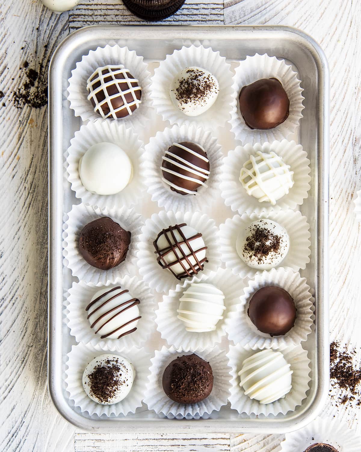 A metal pan topped with chocolate and white chocolate covered Oreo balls in rows in paper liners.