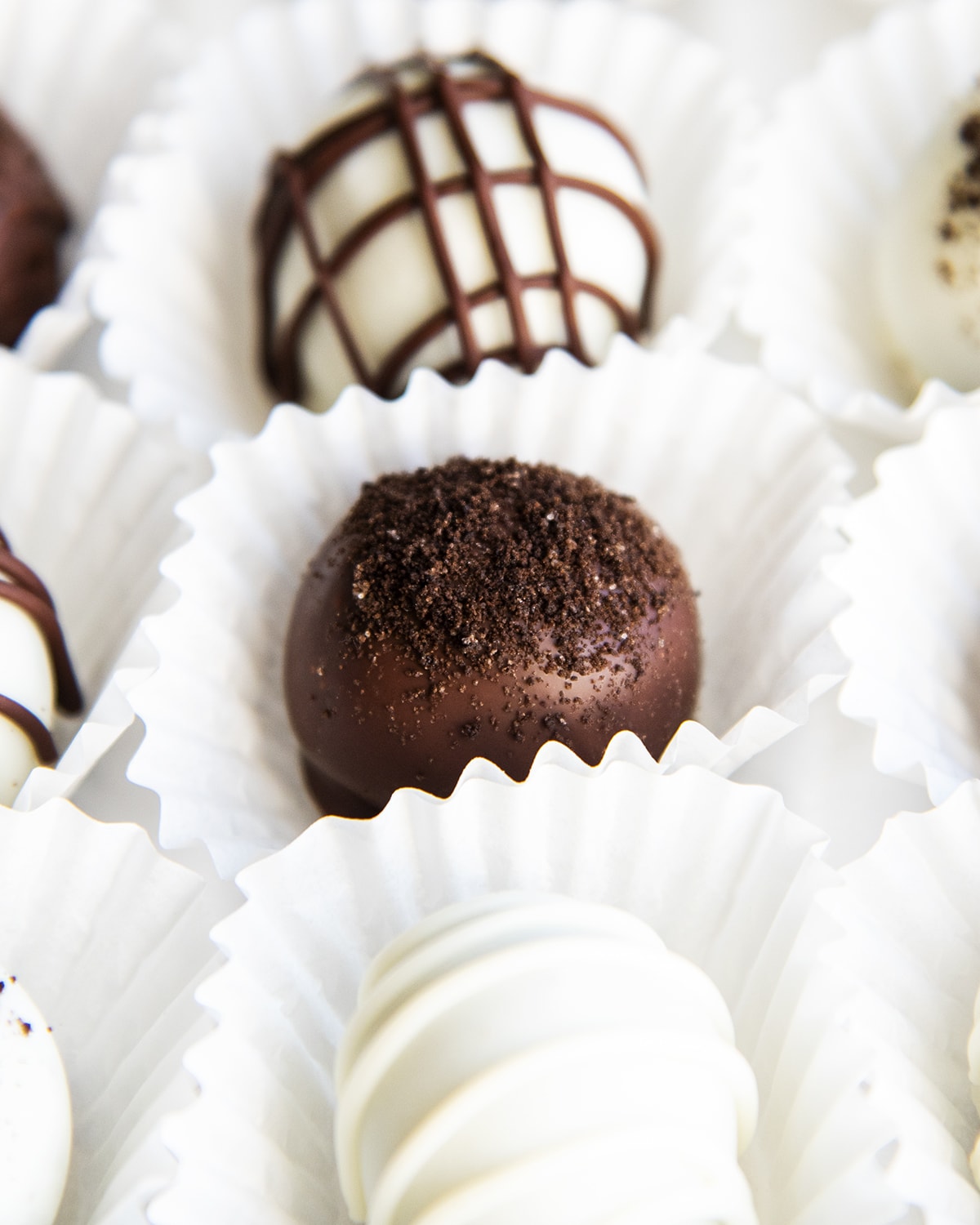A close up of a chocolate covered Oreo ball topped with Oreo crumbs set in a white paper liner.
