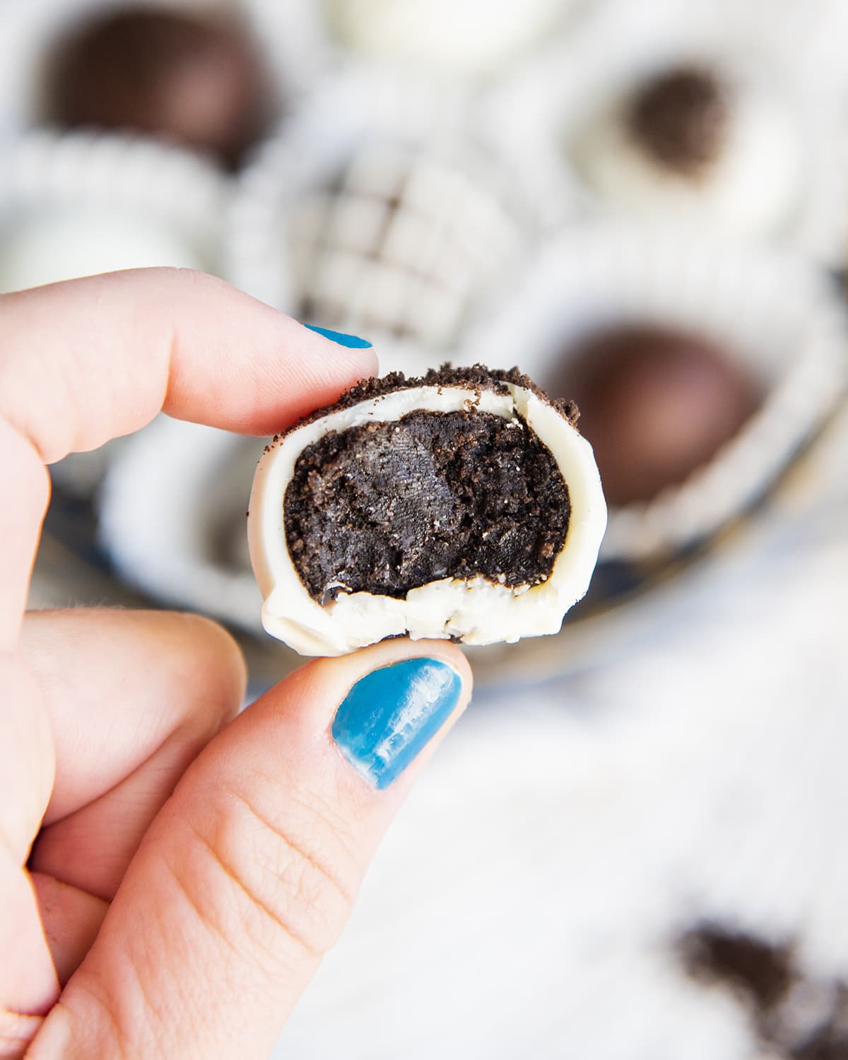 A hand holding a white chocolate Oreo ball with a bite out of it showing the Oreo center.