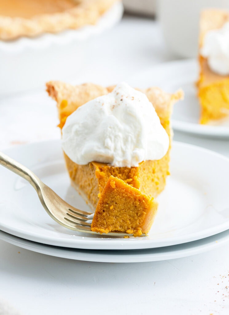 A piece of pumpkin pie with a bite removed, and sitting on a fork on the plate.