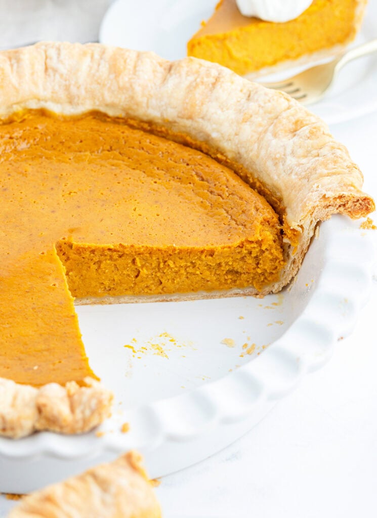 A pumpkin pie in a white pie plate, with a couple pieces removed.