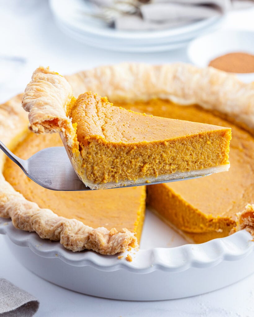 A piece of pumpkin pie on a spatula above the pie.