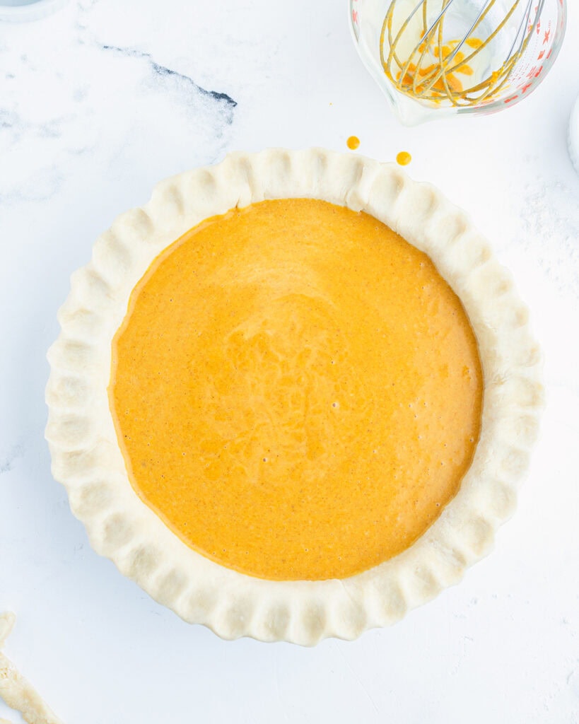 A pie crust filled with a liquid unbaked pumpkin pie filling.
