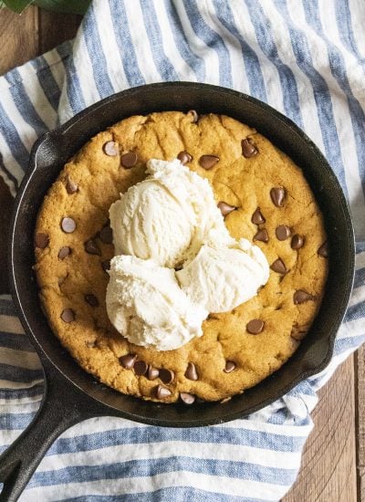 A pumpkin skillet cookie in a black skillet topped with three scoops of vanilla ice cream.