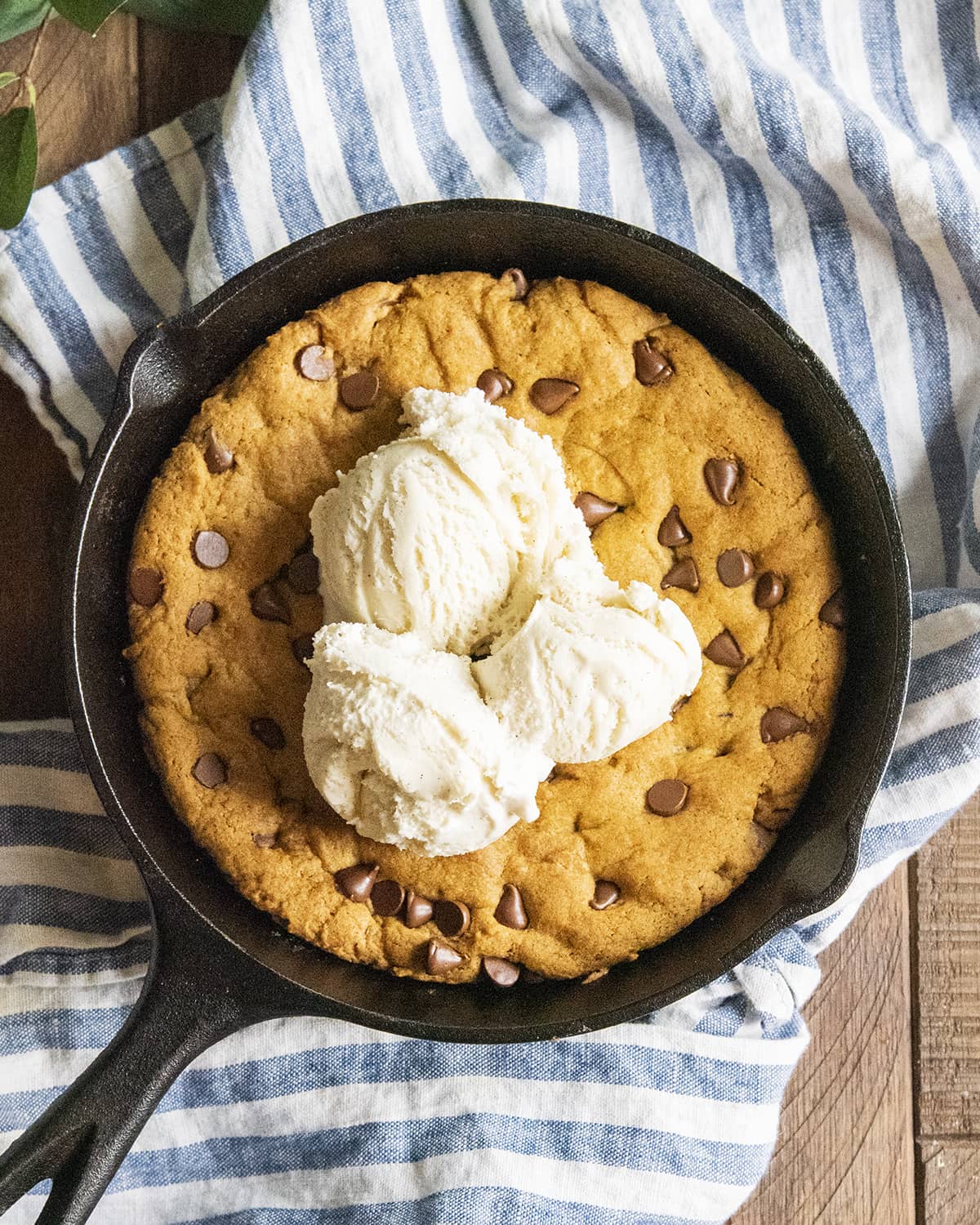 A pumpkin skillet cookie in a black skillet topped with three scoops of vanilla ice cream.