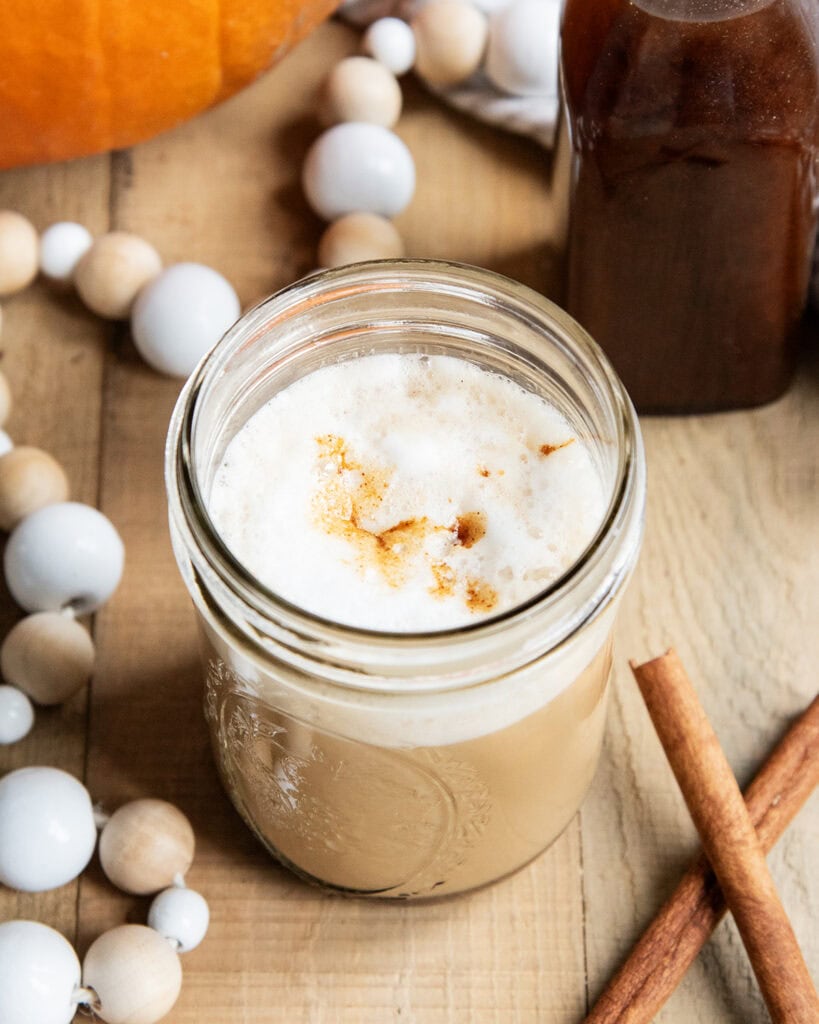 A glass of a homemade pumpkin spice latte with foam on top, topped with pumpkin syrup.