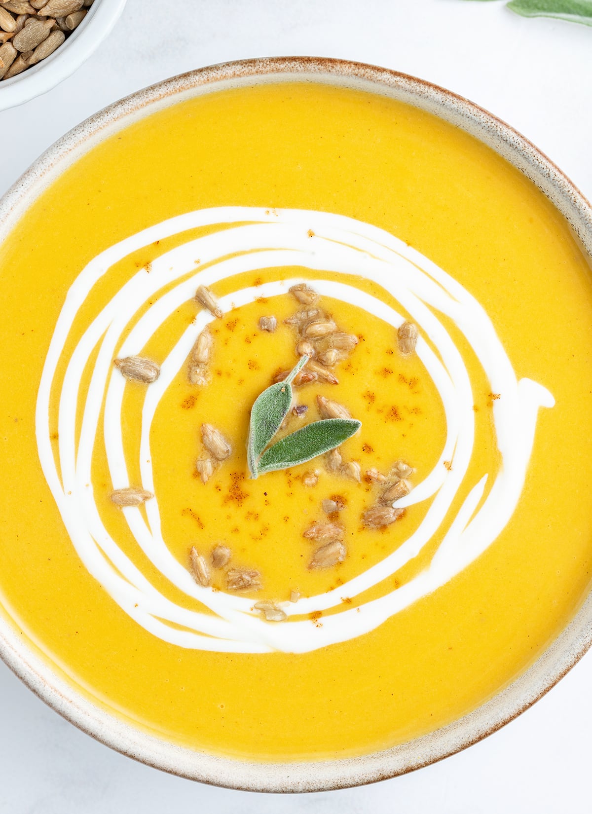 An overhead photo of a bowl of roasted butternut squash soup topped with sunflower seeds and two sage leaves.