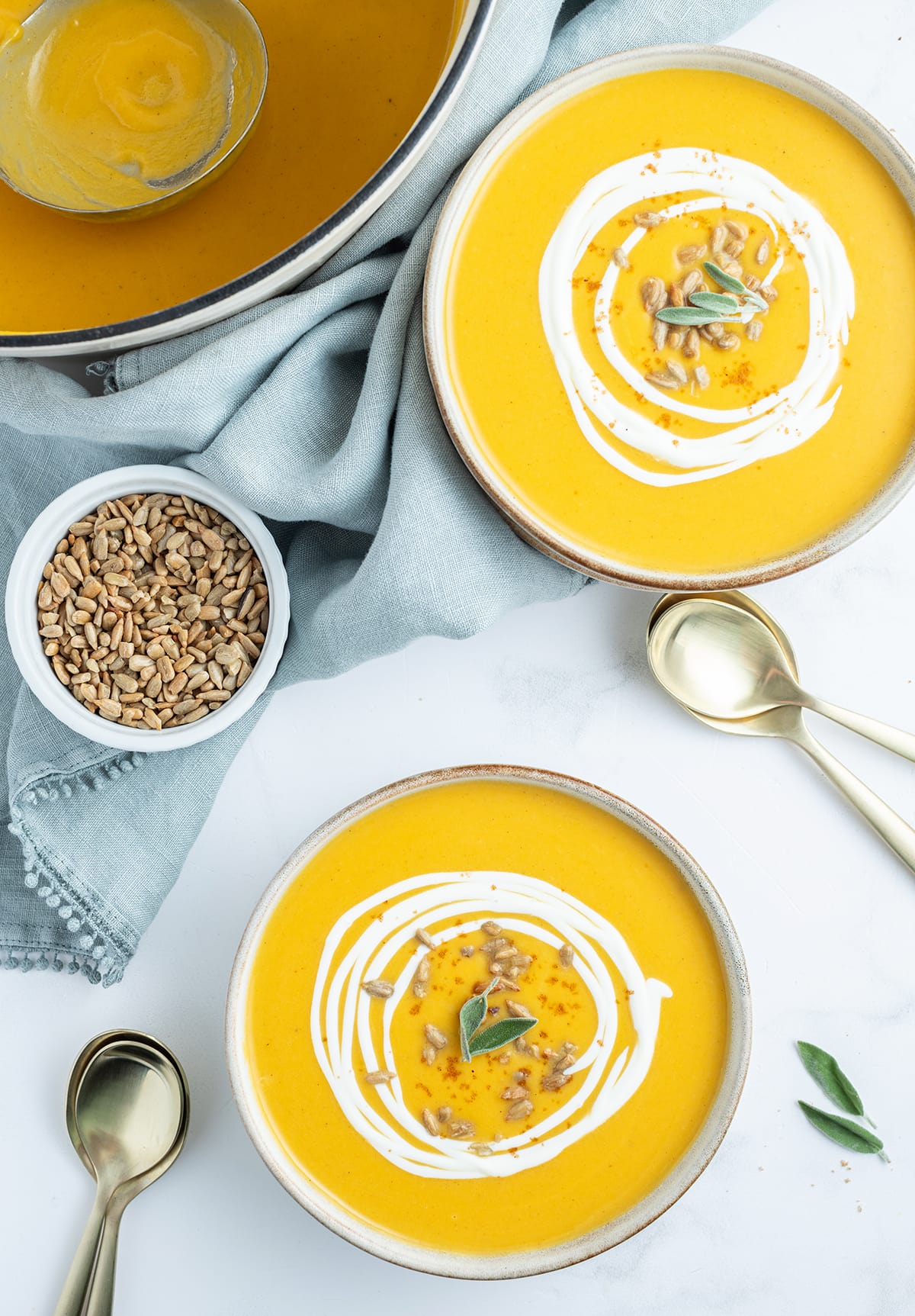 An overhead photo of two bowl of roasted butternut squash soup topped with heavy cream and sunflower seeds.