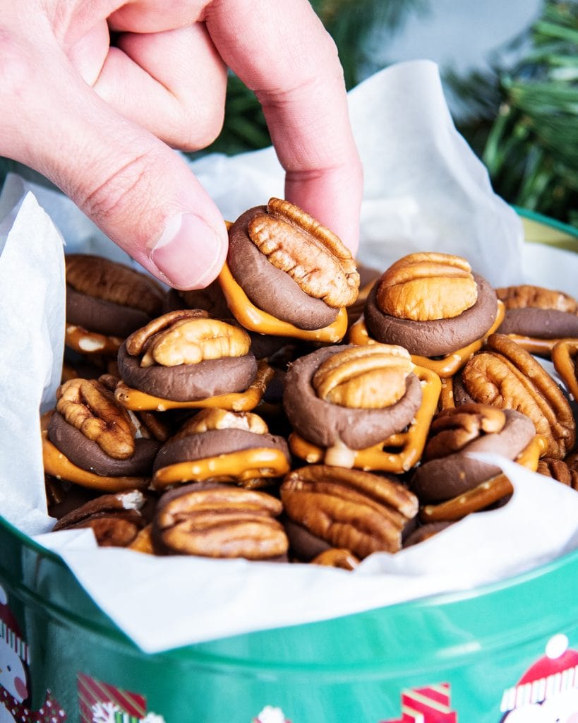 A hand grabbing a pretzel rolo turtle out of a green metal tin.