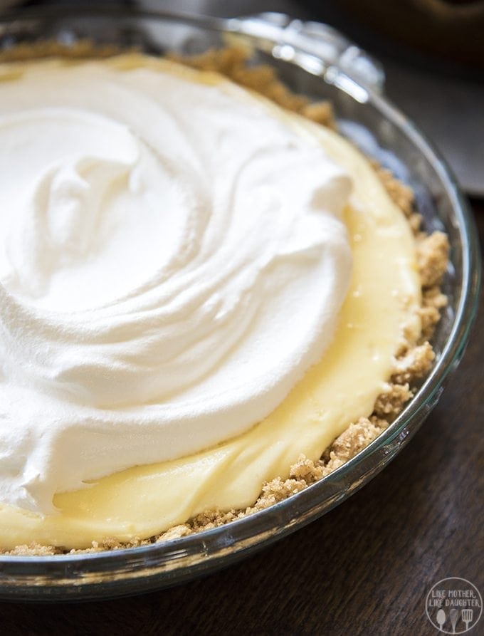 A banana cream pie in a glass pie plate, with a graham cracker crust, yellow pudding filling, and topped with a swirl of whipped cream.