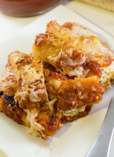 Angled view of chicken parmesan manicotti on a white plate.