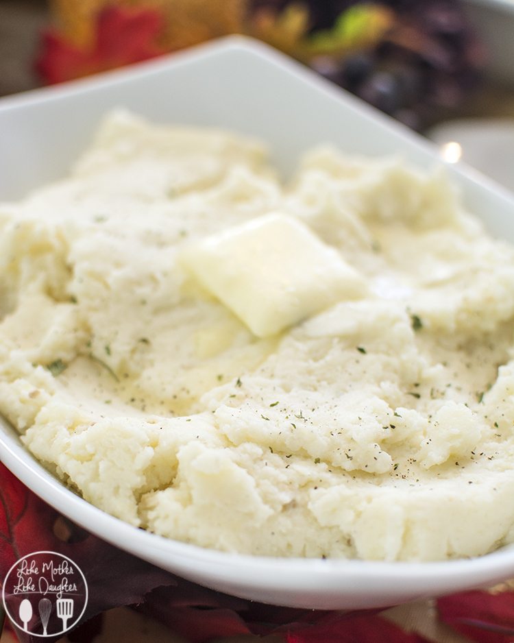 A bowl of homemade mashed potatoes topped with a sprinkle of herbs and a pat of butter.
