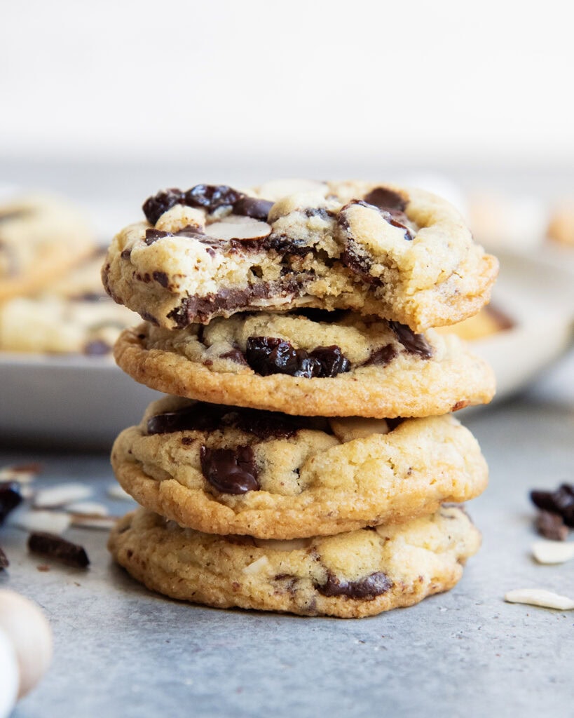 A stack of four cherry almond chocolate chip cookies, and the top cookie has a bite out of it.