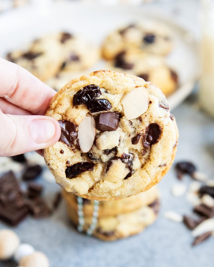 A hand holding a chocolate chip, cherry, almond cookie.