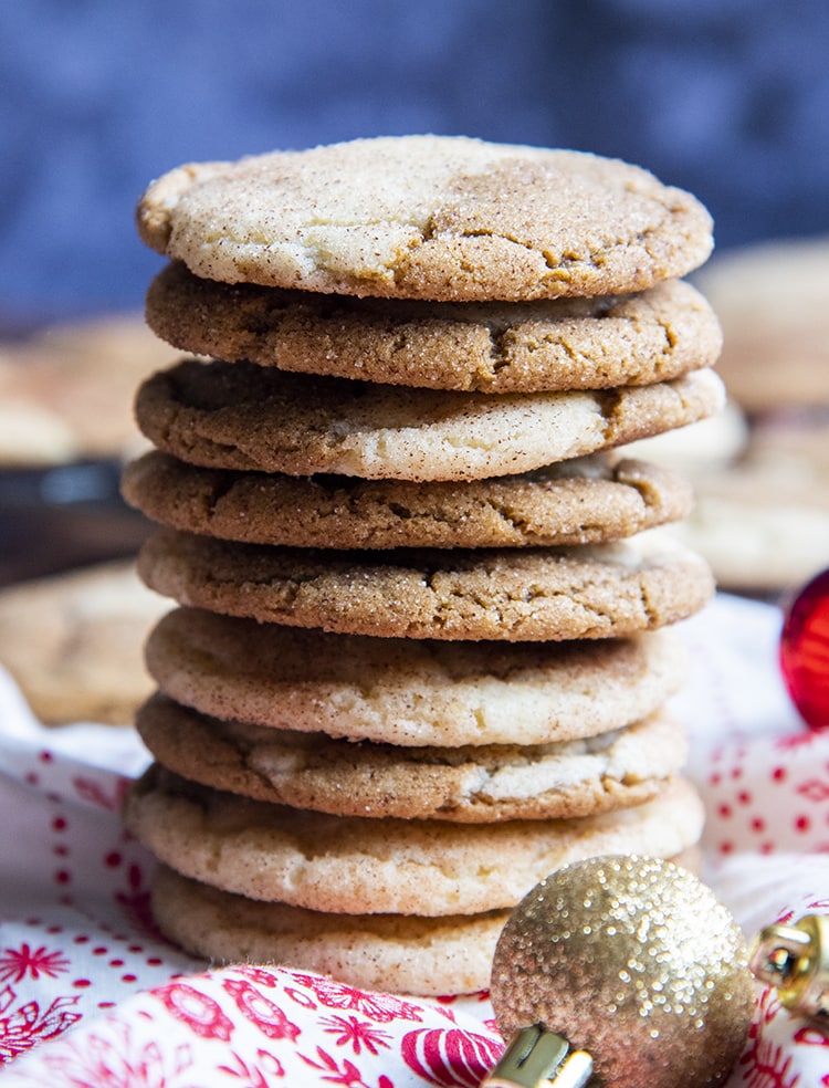 A stack of gingerdoodle cookies, 9 cookies high on a red and white cloth with small Christmas ornaments around.