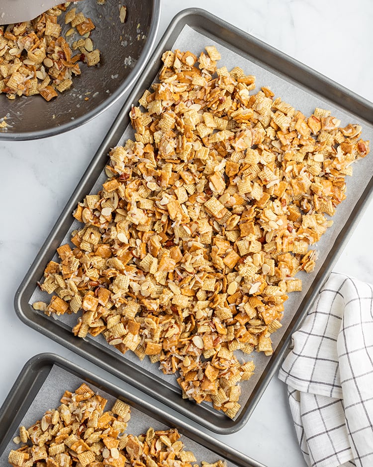 Gooey coconut chex mix on a cookie sheet. It has rice chex, golden grahams, almonds, and coconut.