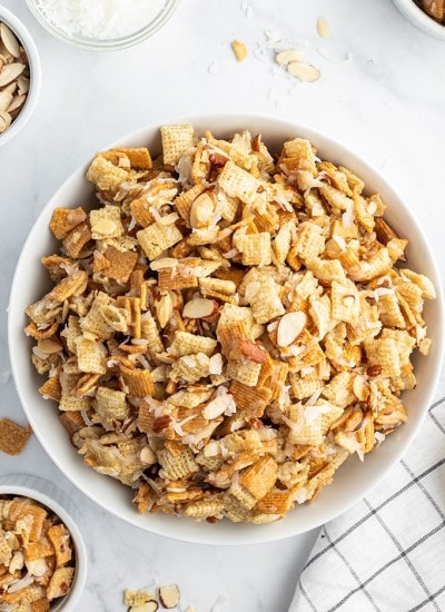 A large bowl of coconut chex mix, that is full of chex, golden grahams, sliced almonds, and shredded coconut.