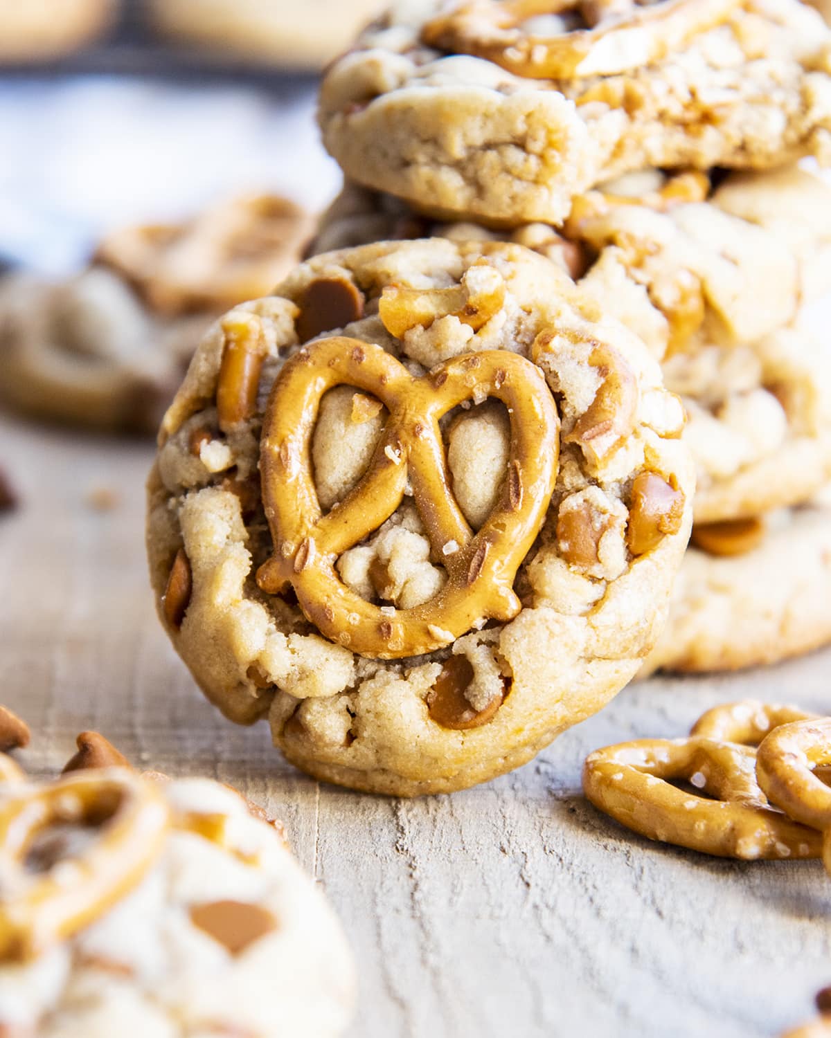 A close up of a cinnamon chip and pretzel cookie topped with a mini pretzel leaning against a stack of cookies.