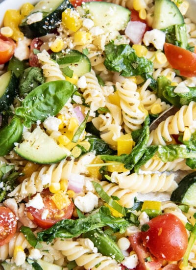 A pasta salad loaded with vegetables and topped with feta crumbles and fresh basil.