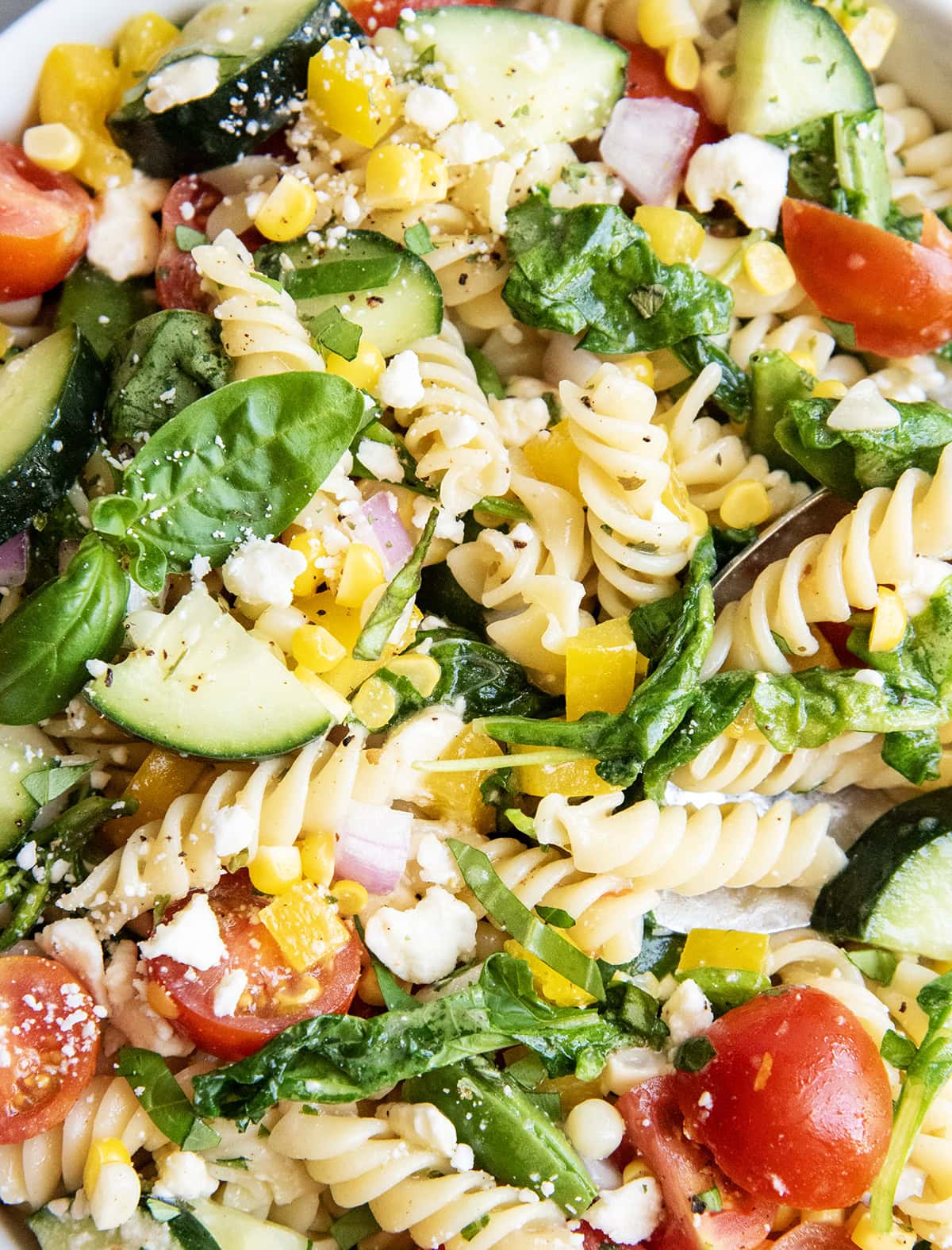 A pasta salad loaded with vegetables and topped with feta crumbles and fresh basil.