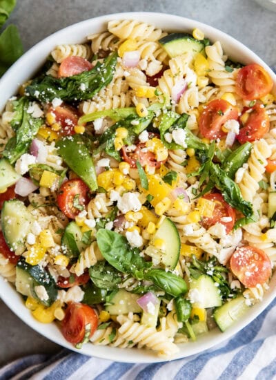 A bowl of pasta with cucumbers, tomatoes, corn and feta.