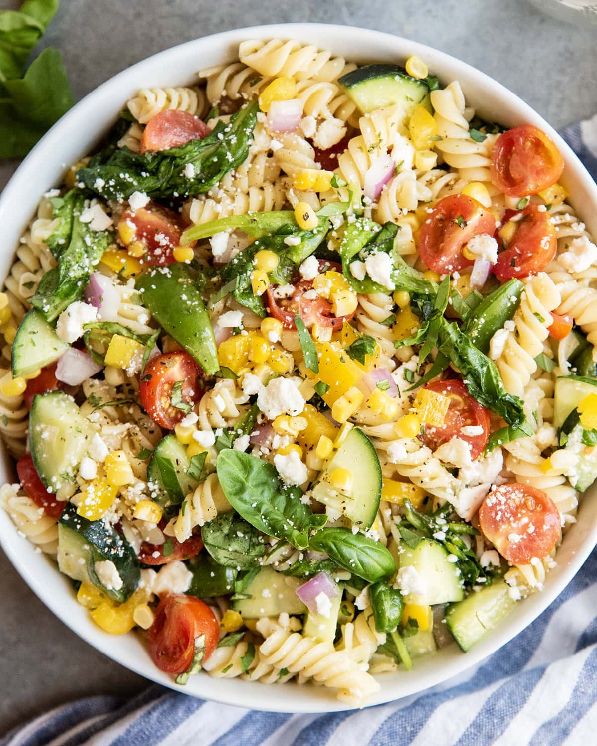 A bowl of pasta with cucumbers, tomatoes, corn and feta.